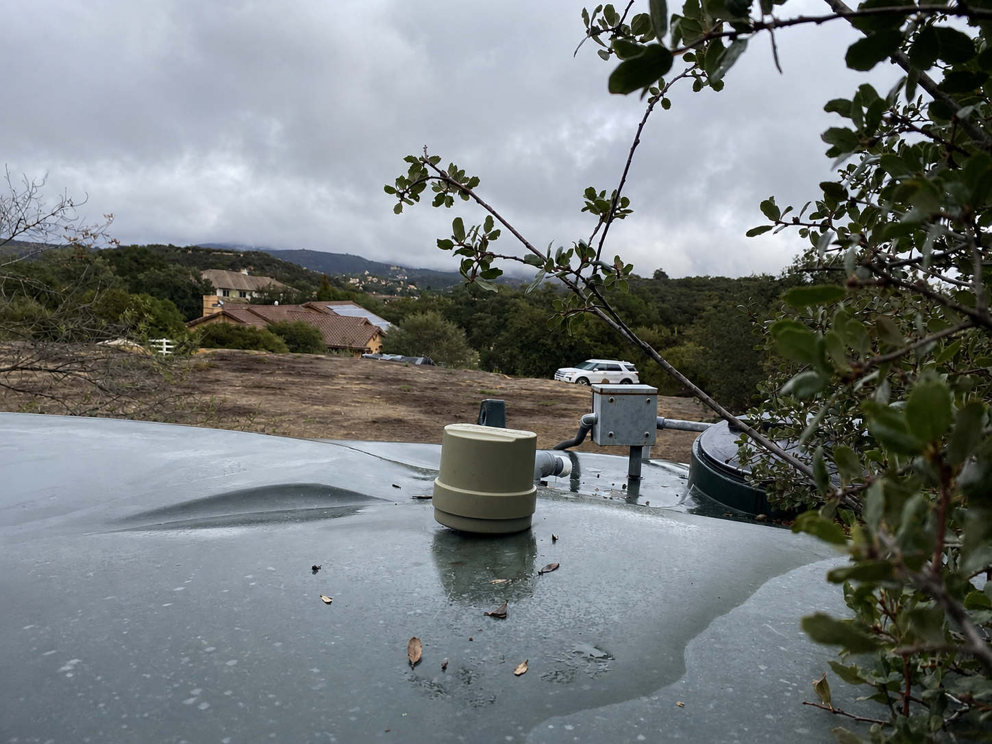 IntelliTank Tank Unit installed on a rain-covered water tank overlooking a home and hillside